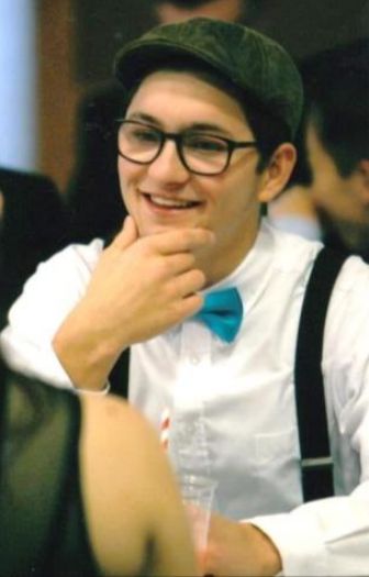 Photo from the 2017 Christmas letter: Theron, smiling with his hand at his chin, in a flat cap, glasses and a teal bow tie