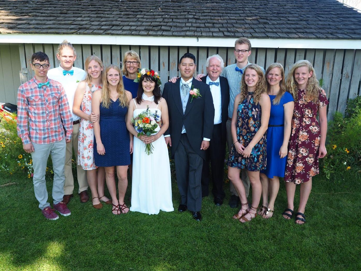 Photo from the 2017 Christmas letter: the wedding party at Brenden and Moeko’s wedding lined up on the grass in front of a gray barn
