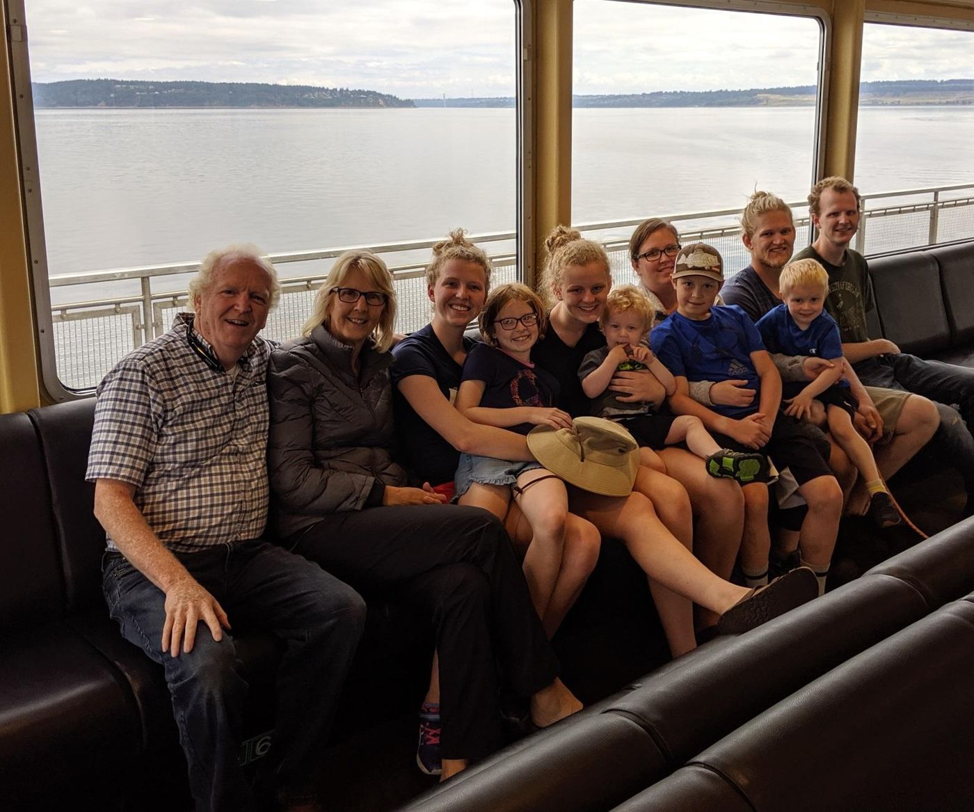 Photo from the 2019 Christmas letter: grandparents, parents and grandchildren seated together on a bench with water visible through the windows behind them